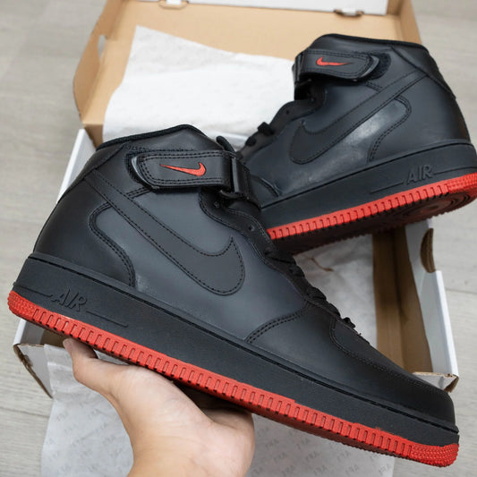 Black high-top sneakers with red soles held in front of a cardboard box.
